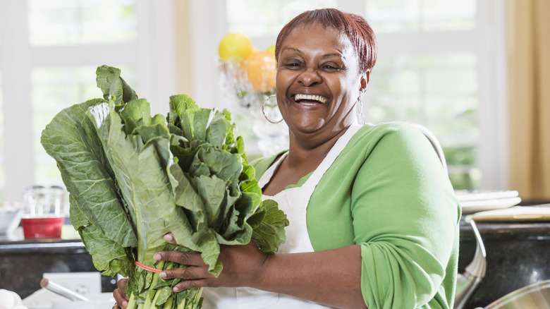 A smiling woman holding a large bunch of collard greens