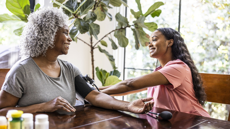 A health care worker checks a woman's blood pressure at home