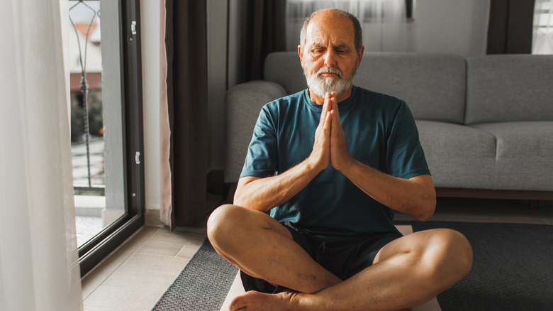 Older man sitting on the floor with palms together in meditation