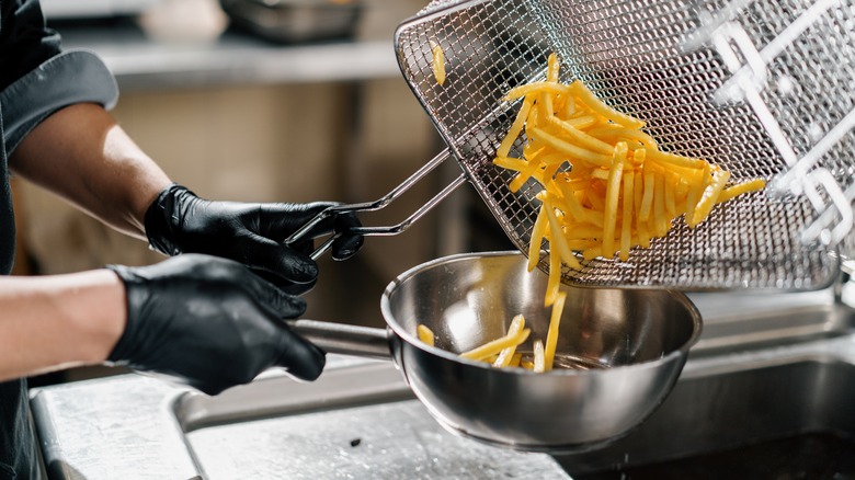 restaurant worker pouring french fries into steel bowl