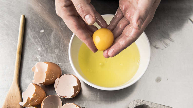 hands holding a yolk over a bowl of egg whites