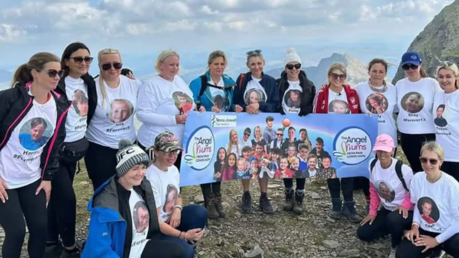 Photo showing a group of mums posing on a mountain with a sign in memory of their children, following their skydive for charity.