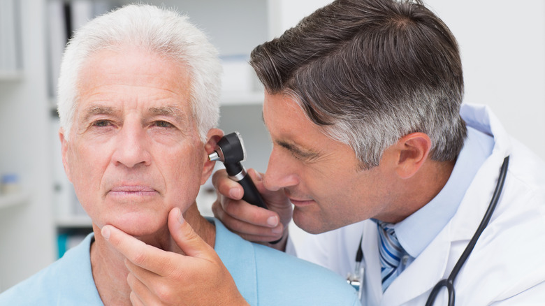 Doctor examining older man's ear