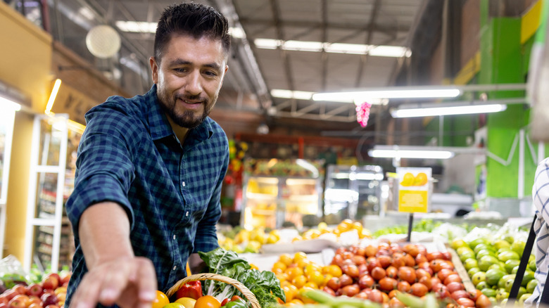 young man reaching for vegetables in produce aisle