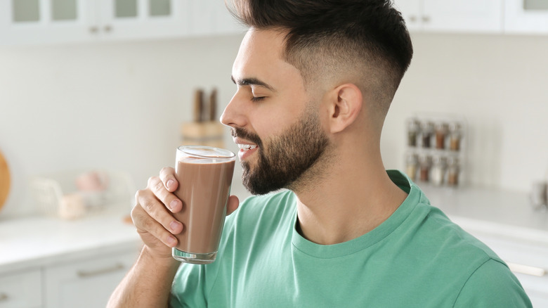 A young man drinking a glass of chocolate milk in the kitchen