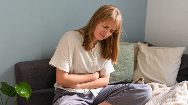 A woman sitting on her couch while holding her stomach