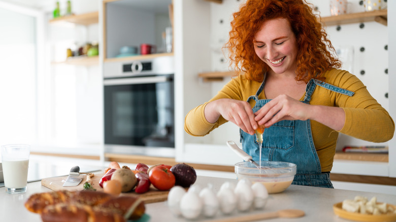 A woman cracking an egg over a glass bowl