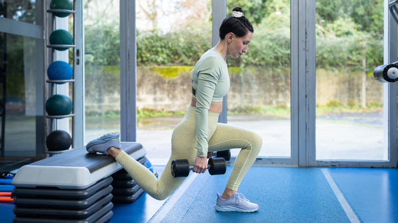 A woman doing Bulgarian split squats using dumbbells