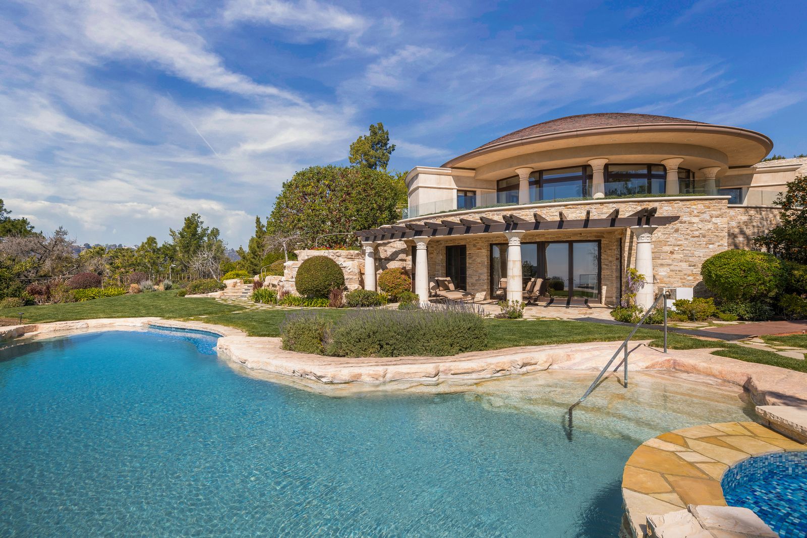 large swimming pool pergola in background poolside rounded stone home