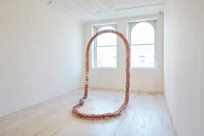 A necklace-like sculpture stood up in a gallery.