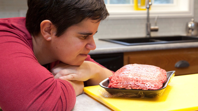 individual stares at ground beef package in kitchen