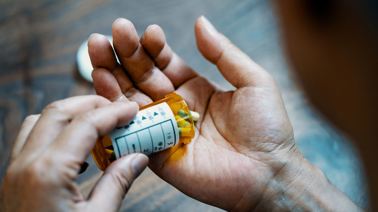 A man's hand holding a medication bottle and some pills
