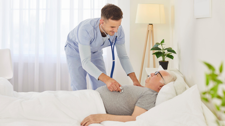 Nurse examining senior male patient lying in bed at home