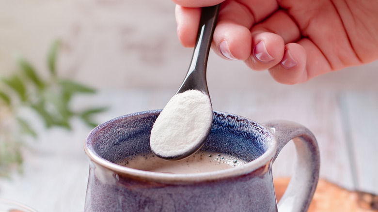 A hand pouring a spoonful of white powder into coffee