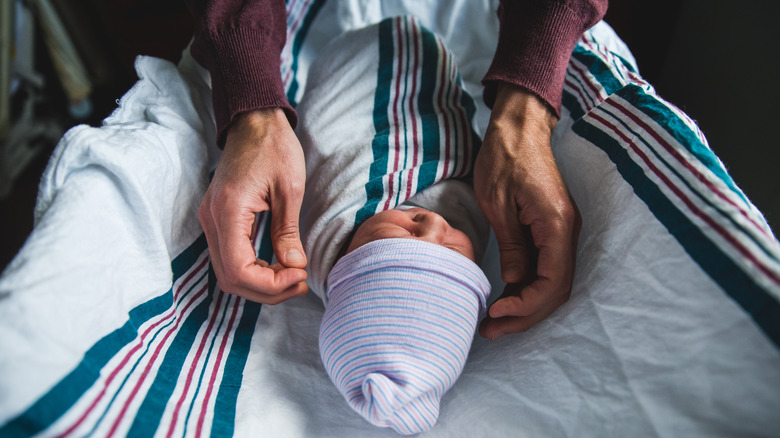 swaddle infant in a little hat with adult arms in frame
