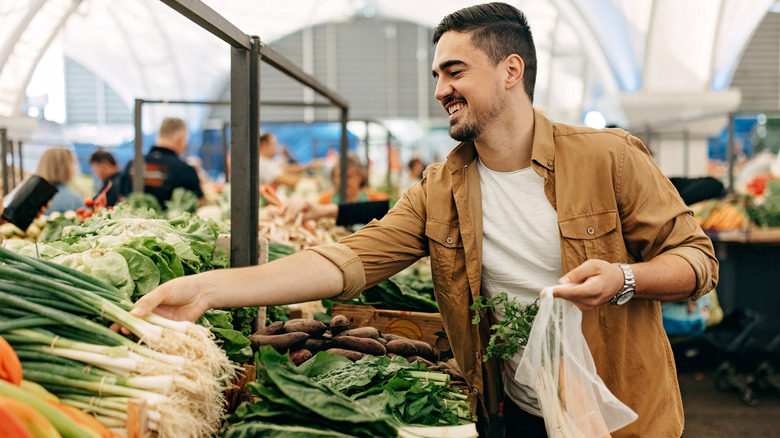 A smiling man choosing vegetables at a market