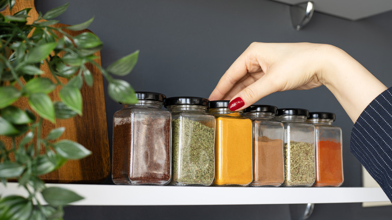 A woman's hand reaching for a jar of turmeric from her spice race