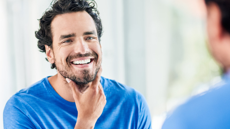 A smiling man touching his skin while looking in the mirror