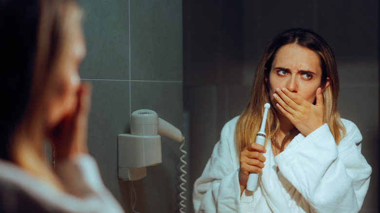 woman covering her mouth while brushing her teeth