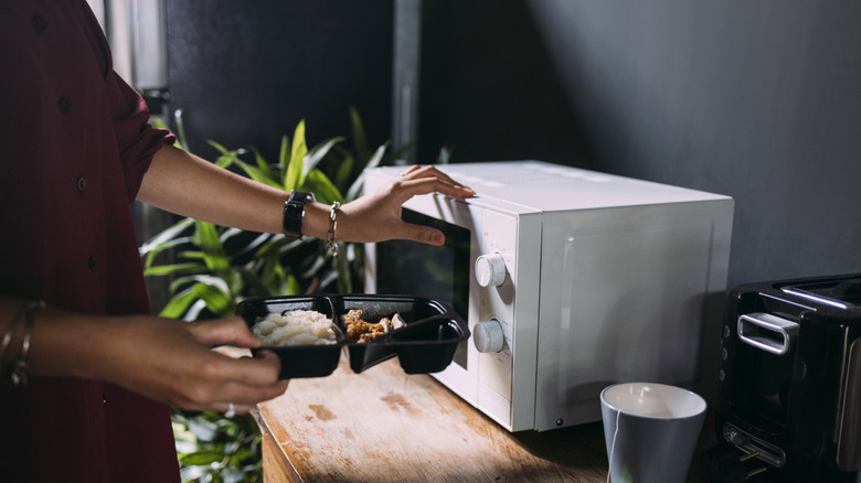 woman putting plastic takeout container in microwave
