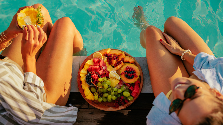 women eating tropical fruits by the pool